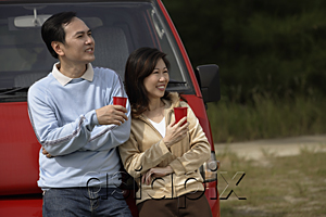 AsiaPix - Man and woman leaning against red van, drinks in hand, camping, outdoors