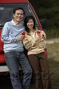 AsiaPix - Man and woman leaning against red van, smiling at camera, camping