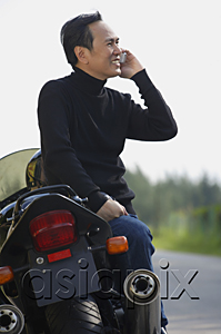 AsiaPix - Mature man leaning on motorcycle, talking on mobile phone