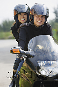 AsiaPix - Man and woman riding motorcycle, wearing helmets, looking at camera