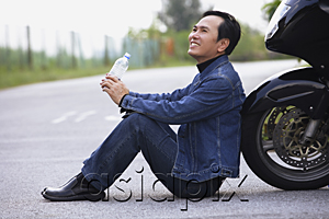 AsiaPix - Man leaning against motorcycle, sitting on road drinking water