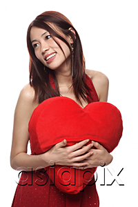 AsiaPix - Young woman holding red heart shaped pillow, looking away