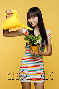 AsiaPix - Young woman watering plant with bright yellow watering can