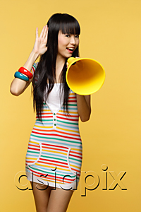 AsiaPix - Young woman talking through yellow megaphone, hand to ear