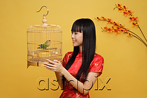 AsiaPix - Young woman holding lovebird in bird cage