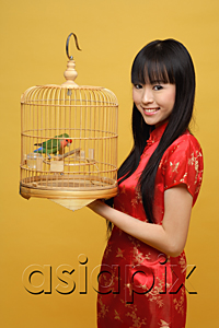 AsiaPix - Young woman holding lovebird in bird cage, smiling