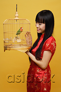 AsiaPix - Young woman holding lovebird in bird cage, looking at bird