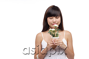 AsiaPix - Young woman wearing white dress, holding small plant and smelling flower