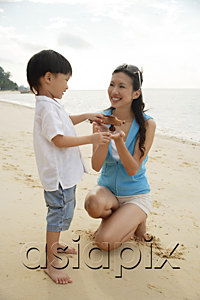 AsiaPix - Mother and son on beach, boy holding wooden airplane