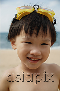 AsiaPix - Young boy on beach with yellow swimming goggles on head, smiling, portrait