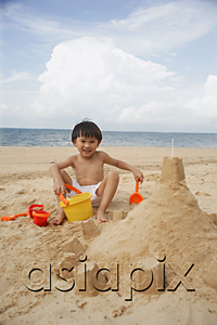 AsiaPix - Young boy on beach building sand castle, smiling