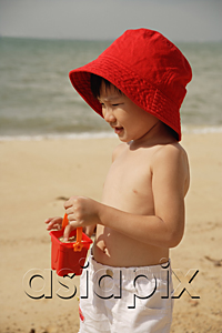 AsiaPix - Young boy on beach, wearing red hat and carrying red beach bucket