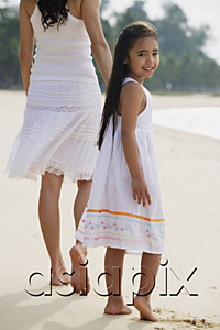 AsiaPix - Mother and daughter walking down beach, daughter looking back towards camera smiling