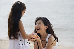 AsiaPix - Mother and daughter on beach, daughter handing conk shell to mother, smiling