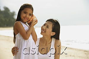 AsiaPix - Mother and daughter on beach, daughter with conk shell to ear listening to ocean