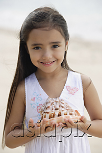 AsiaPix - Young girl on beach holding giant conk shell in her hands, smiling