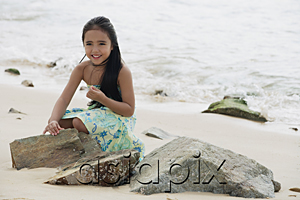 AsiaPix - Young girl sitting on beach by rocks