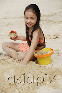 AsiaPix - Young girl building sand castle on beach, smiling