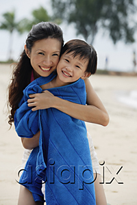 AsiaPix - Mother hugging son on beach, son wrapped in blue towel