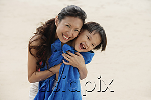 AsiaPix - Mother hugging son on beach, son wrapped in blue towel, smiling