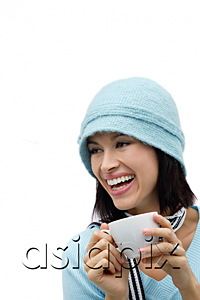 AsiaPix - Young woman wearing wool hat and scarf, holding mug and laughing