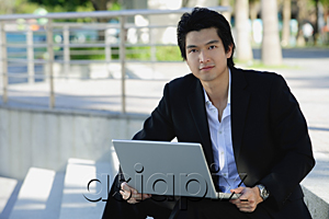 AsiaPix - A man uses his laptop outdoors while he looks at the camera