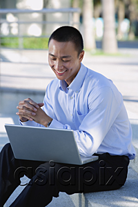 AsiaPix - A man smiles as he uses his laptop outdoors