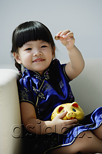 AsiaPix - A small girl in blue silk cheongsam plays with a piggy bank