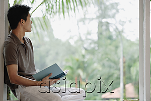 AsiaPix - A man holds a book as he looks out a window