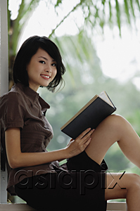 AsiaPix - A woman smiles at the camera as she reads a book