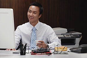 AsiaPix - A man has a hot drink while he works at his desk