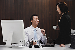 AsiaPix - A man sits at his desk while he talks with a woman at work