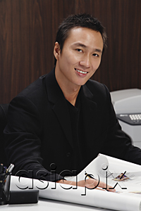 AsiaPix - A man smiles at the camera as he rolls out plans on his desk
