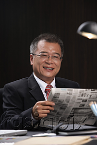 AsiaPix - A man smiles at the camera as he reads the newspaper at work
