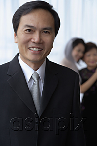AsiaPix - A man smiles at the camera while a bride and her mother hug in the background