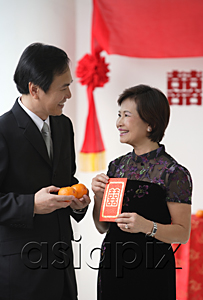 AsiaPix - A couple smile as they hold two oranges and a red envelope