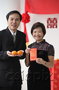 AsiaPix - A couple look at the camera as they hold two oranges and a red envelope