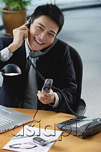 AsiaPix - A man smiles at the camera as he sits at his desk which has lots of phones on it