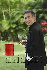 AsiaPix - Man in traditional clothing, standing in park holding Chinese lantern