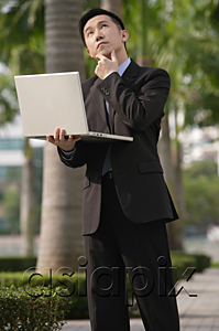 AsiaPix - Businessman with quizzical expression, holding laptop and looking up