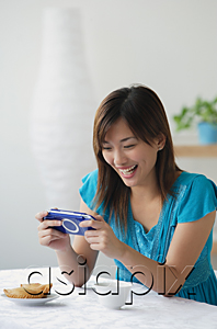 AsiaPix - Young woman playing on handheld game console