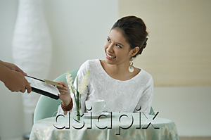 AsiaPix - Young woman sitting in restaurant, being handed a menu