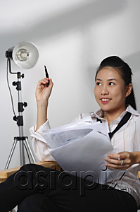 AsiaPix - Young woman sitting with paper and pen looking into distance