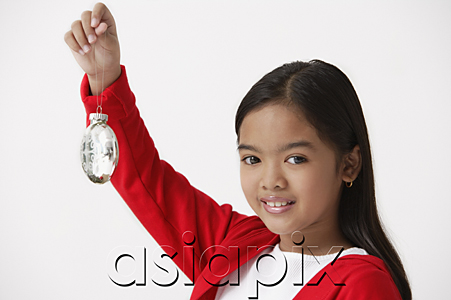 AsiaPix - Girl holding up Christmas ornament looking at camera