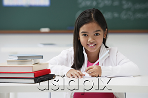 AsiaPix - Girl with pen sitting at school desk smiling at camera