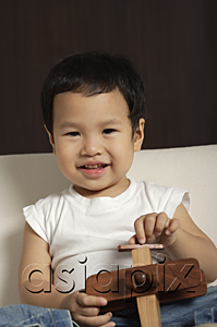 AsiaPix - Baby boy holding wooden toy plane smiling at camera