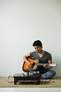 AsiaPix - Young man sitting on floor and playing guitar
