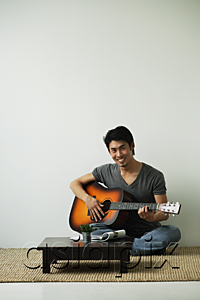 AsiaPix - Young man sitting on floor playing guitar smiling at camera