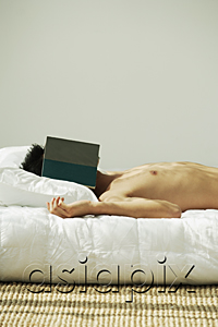 AsiaPix - Young man lying in bed, face covered by a book