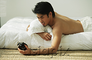 AsiaPix - Young man lying in bed, holding alarm clock